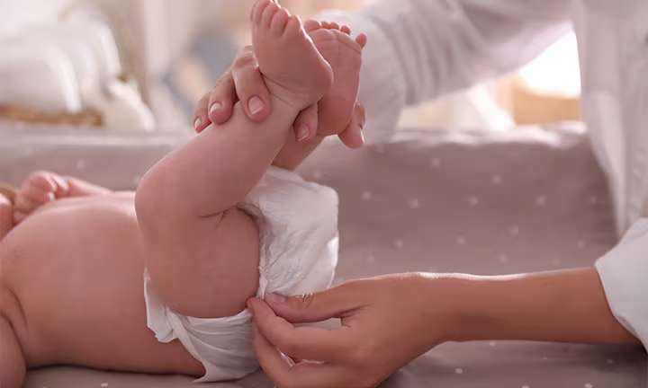 A baby lying on a changing pad while a caregiver adjusts their diaper