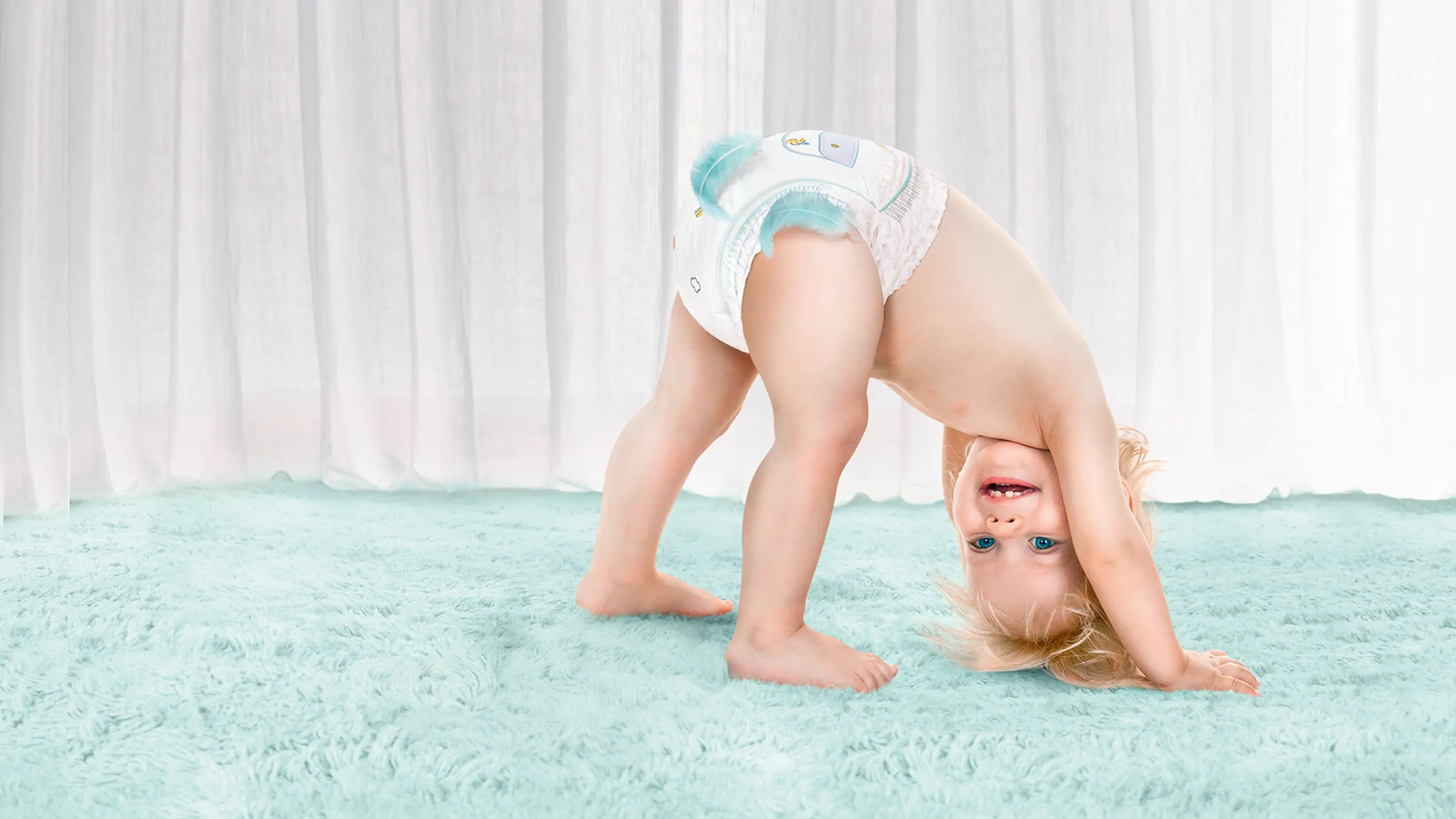 Usmívající se miminko s hlavou dolů, které má na sobě Pampers Pants