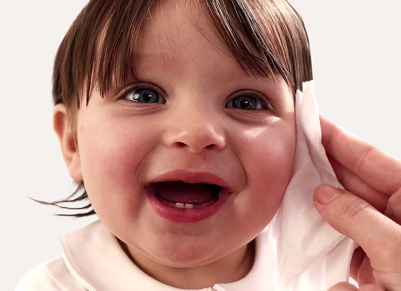 Um close-up do rosto de um bebé enquanto uma mão lhe limpa suavemente a bochecha com uma toalhita Dodot.