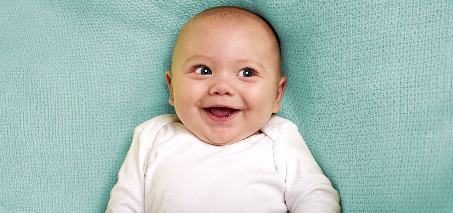 Smiling baby in a white onesie on a soft blue blanket.