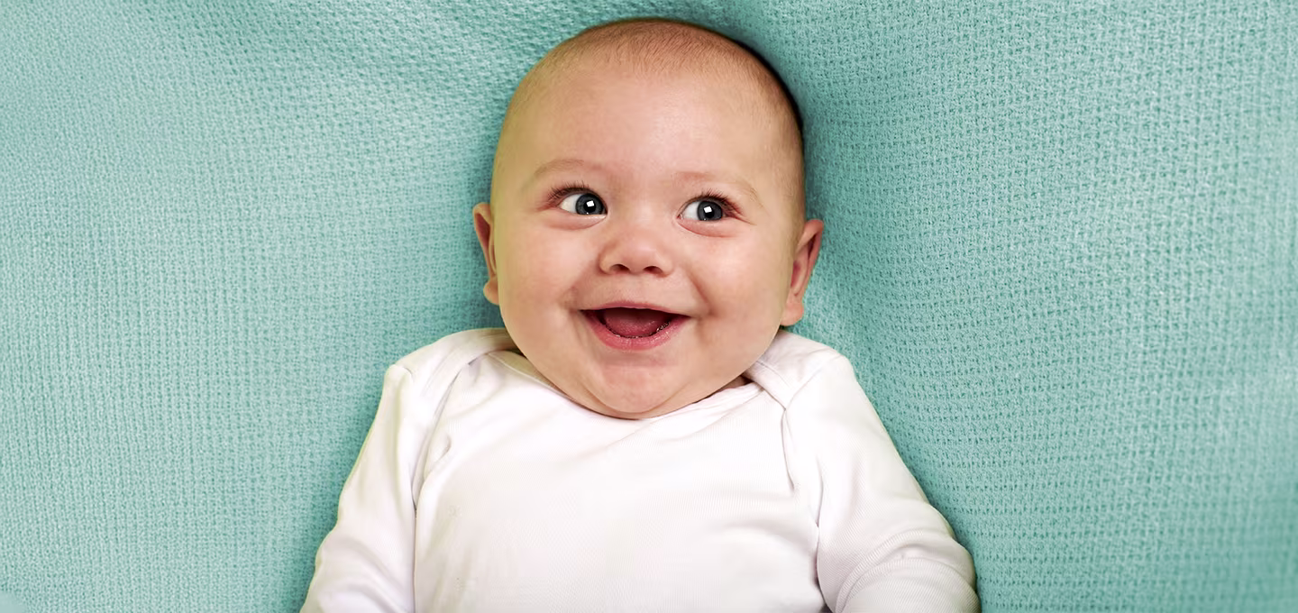 Smiling baby in a white onesie on a soft blue blanket.