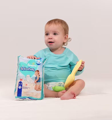 A joyful baby proudly holding a pack of Pampers Splashers, ready for a fun day at the pool with their spade!