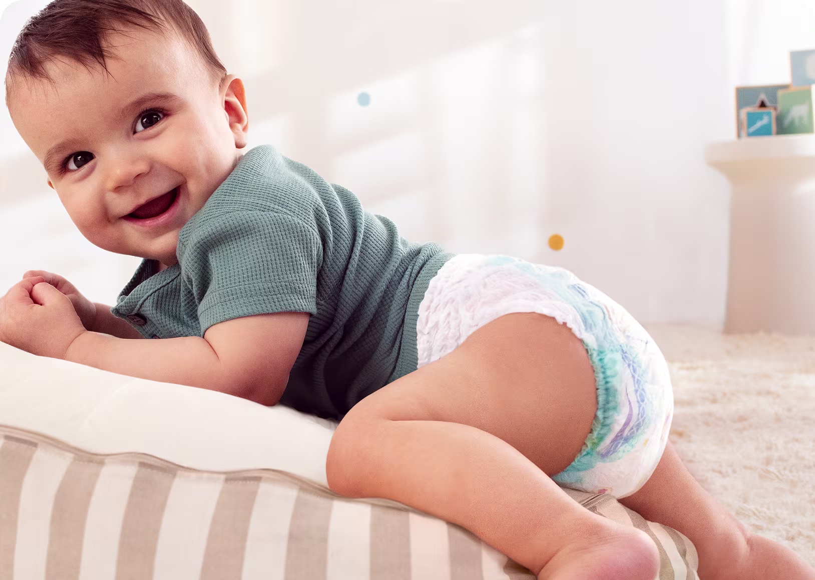 Een baby met een Pampers Pants kruipt op een gestreept kussen. Een baby met een Pampers Pants kruipt op een gestreept kussen.