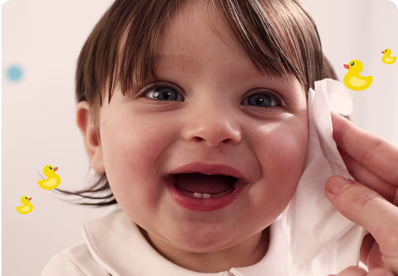 Smiling baby in a high chair, face covered in spaghetti sauce, holding a spoon