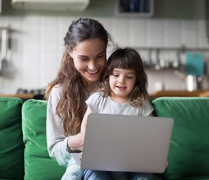 Parenting in the Digital Age: How Tech-Savvy Are You? Smiling mother and child using a laptop together on a green couch in a cozy living room.