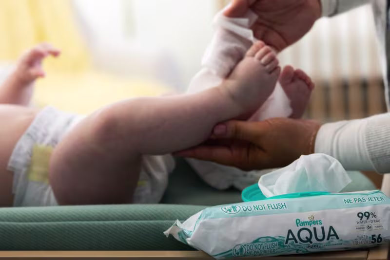 Aqua Pure wipes with mom in the background changing babys diaper