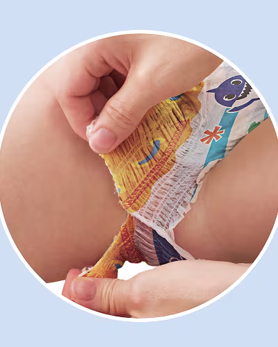 Um close-up mostra as mãos de um pai a rasgar a lateral de uma fralda de natação com tema Baby Shark num bebé, destacando a característica de “Laterais super fáceis de rasgar”.