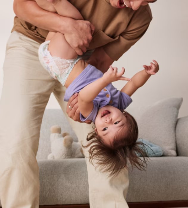 Image of a dad and his toddler both smiling and sharing a playful moment as he holds her carefully upside down
