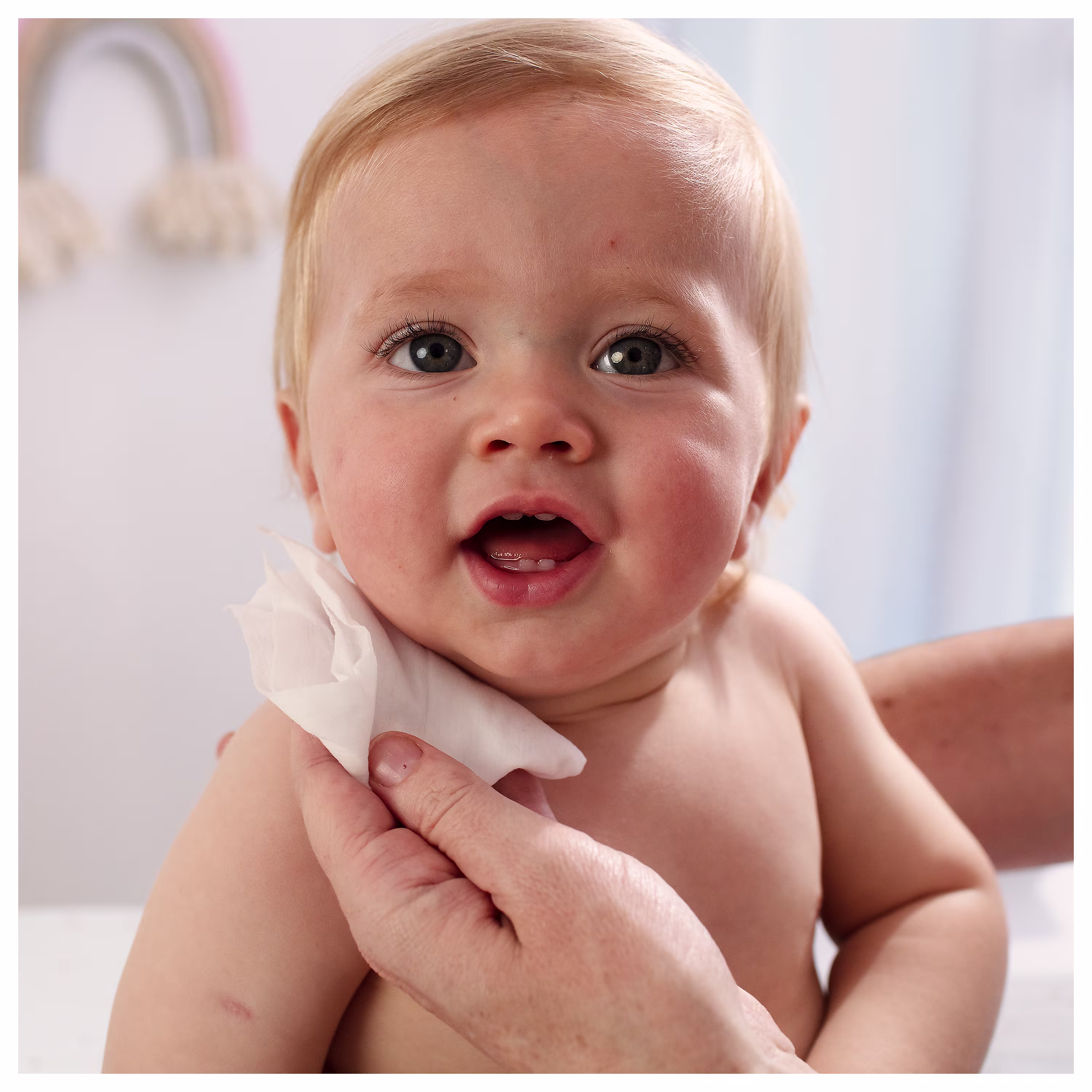 Un prim-plan al feței unui bebeluș, în timp ce o mână îi curăță ușor obrazul cu o șervețel umed Pampers 99% Water.