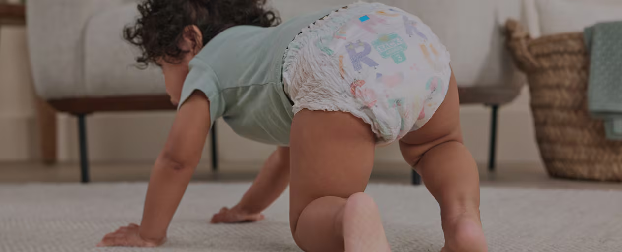 A baby dressed in teal tshirt and pampers diaper pants seen crawling on a carpet