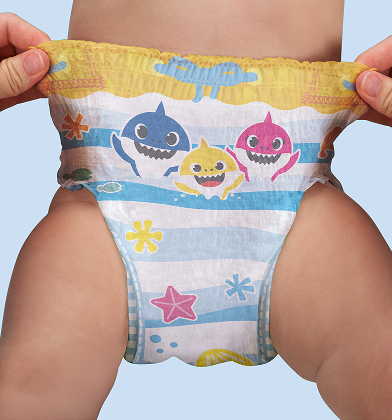 Un par de manos estira los lados de un pañal de natación con temática de Baby Shark en la parte inferior de un bebé, mostrando la cinturilla elástica y el diseño completo.