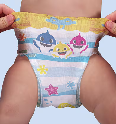 Un par de manos estira los lados de un pañal de natación con temática de Baby Shark en la parte inferior de un bebé, mostrando la cinturilla elástica y el diseño completo.