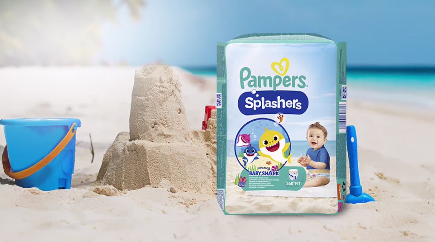Een pak Pampers® Splashers zwemluiers op het strand, omringd door strandspeelgoed.