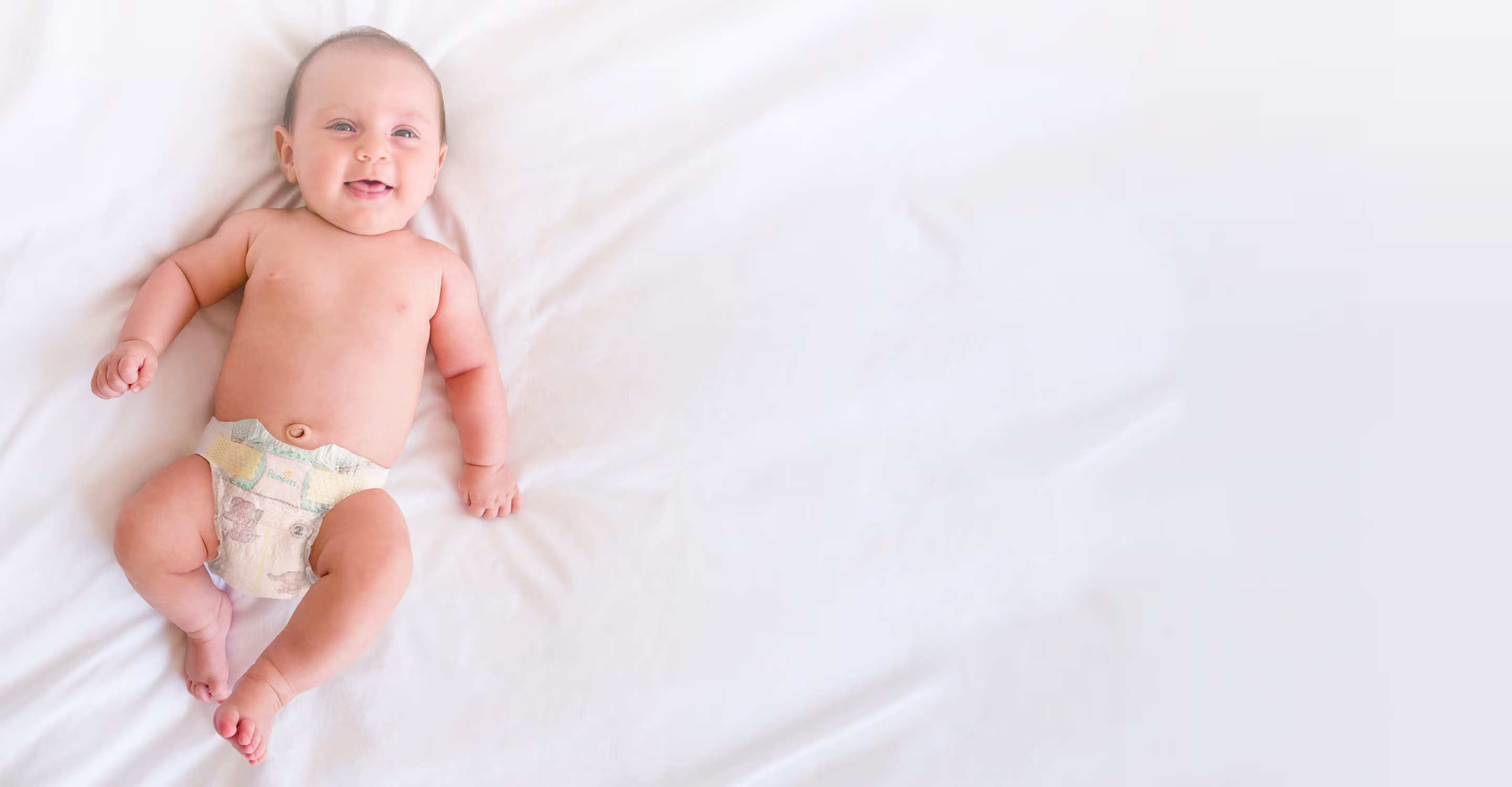Een baby ligt op een deken en draagt een Pampers Premium Protection luier.