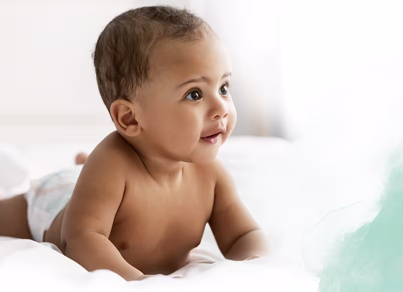 Pachetul Pampers Harmonie stă pe burtă pe un cearșaf alb.