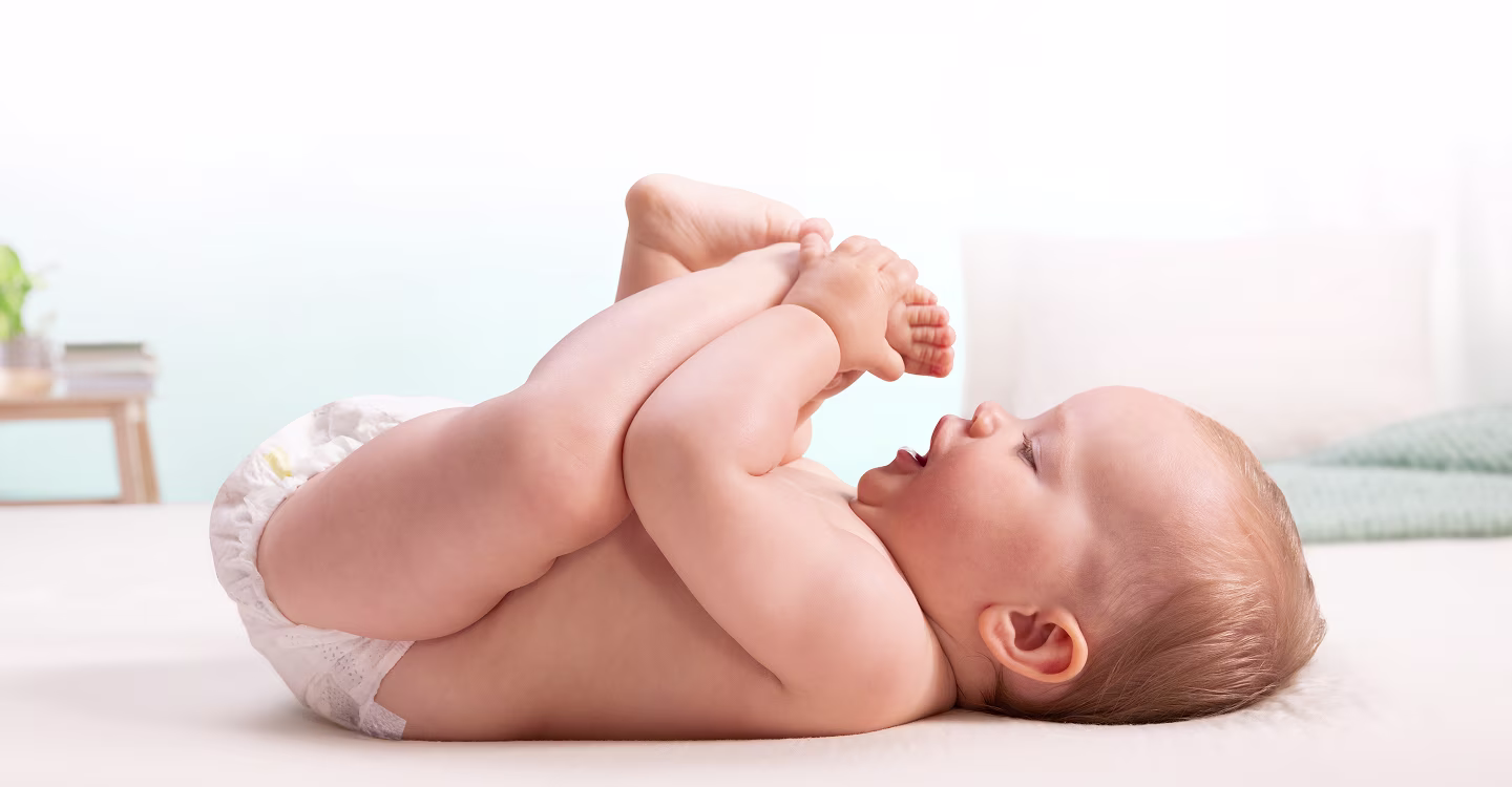 En baby ligger på ryggen og leker glad med føttene sine.