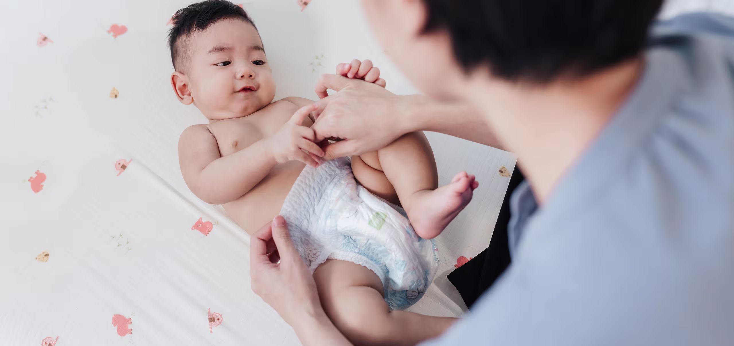 Bebê deitado de costas em um sofá cinza, com um adulto segurando delicadamente seus pés.