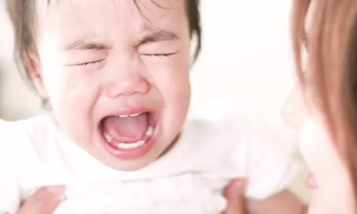 Ein Baby mit Dreimonatskoliken weint im Arm der Mutter