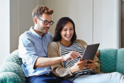 Smiling couple sitting on a couch, browsing a tablet together.