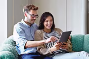 Smiling couple sitting on a couch, browsing a tablet together.