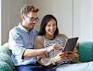 Smiling couple sitting on a couch, browsing a tablet together.
