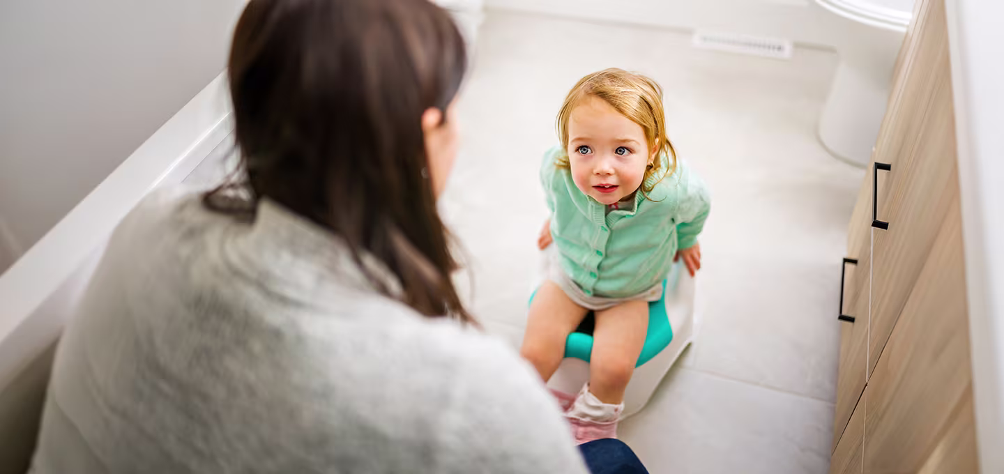A toddler sitting on a potty, looking up at their caregiver