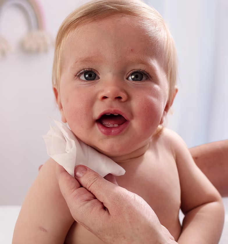 Un gros plan du visage d’un bébé pendant qu’une main nettoie doucement sa joue avec une lingette Pampers 99% Water. Un gros plan du visage d’un bébé pendant qu’une main nettoie doucement sa joue avec une lingette Pampers 99% Water.
