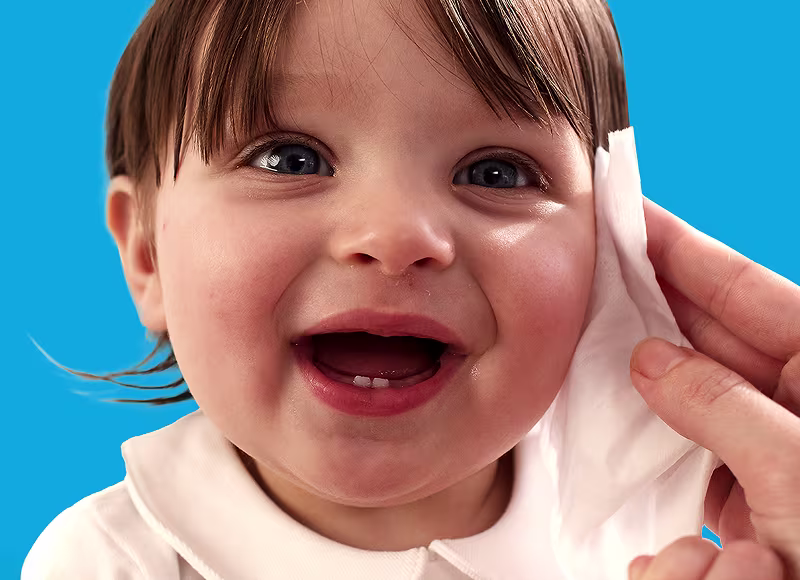 Um primeiro plano do rosto de um bebé enquanto uma mão lhe limpa suavemente a bochecha com uma toalhita Dodot.