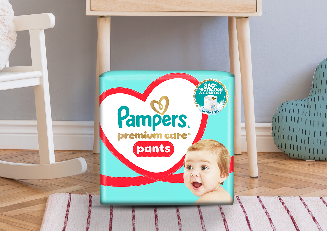 Interiorul unei camere de bebeluși în care se vede pătuțul și pachetul de Pampers Premium Care Pants.