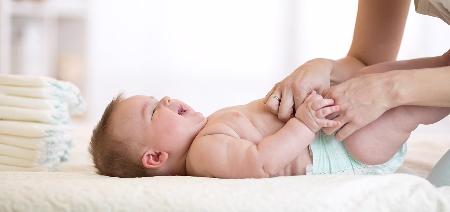 Mother changing the diaper on her baby, soft environment with a diaper stack in the background