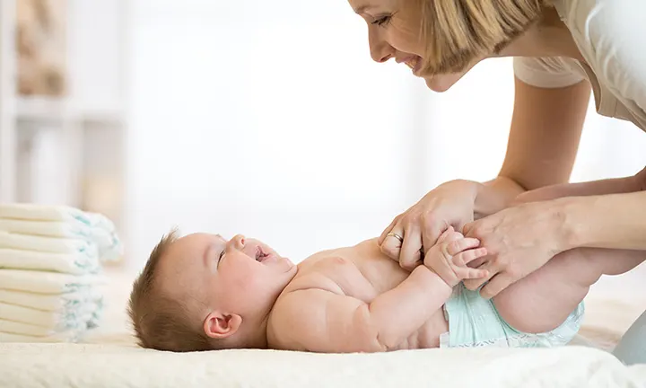 Mother changing the diaper on her baby, soft environment with a diaper stack in the background