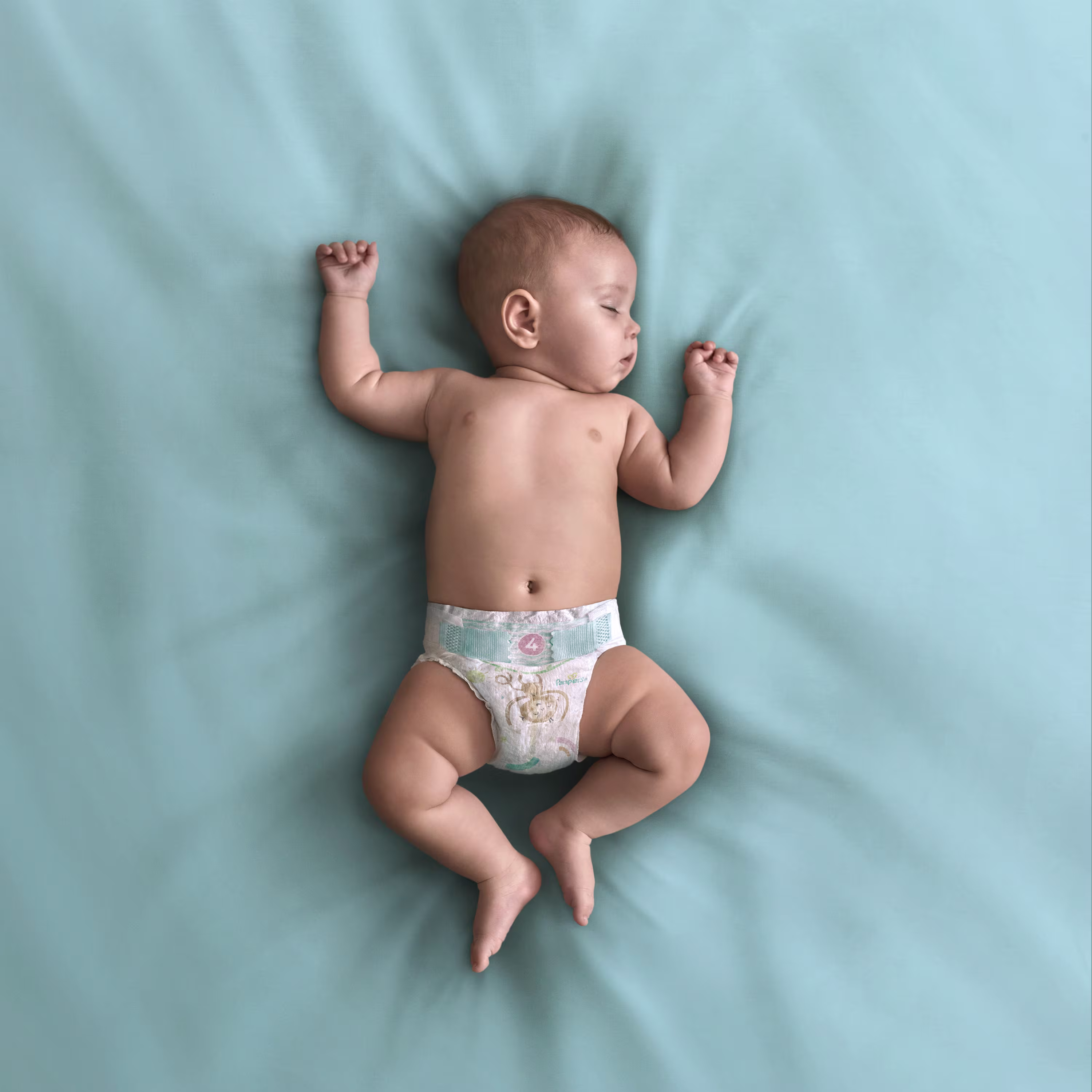 Ein Baby liegt auf dem Rücken auf einer türkisenen Decke und trägt eine Pampers Baby-Dry Windel