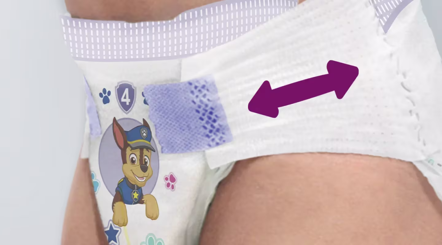 Se muestra un primer plano del costado de un bebé que lleva un pañal. Una flecha morada indica que se puede tirar de la pestaña elástica, y el pañal está ajustado al cuerpo del bebé.