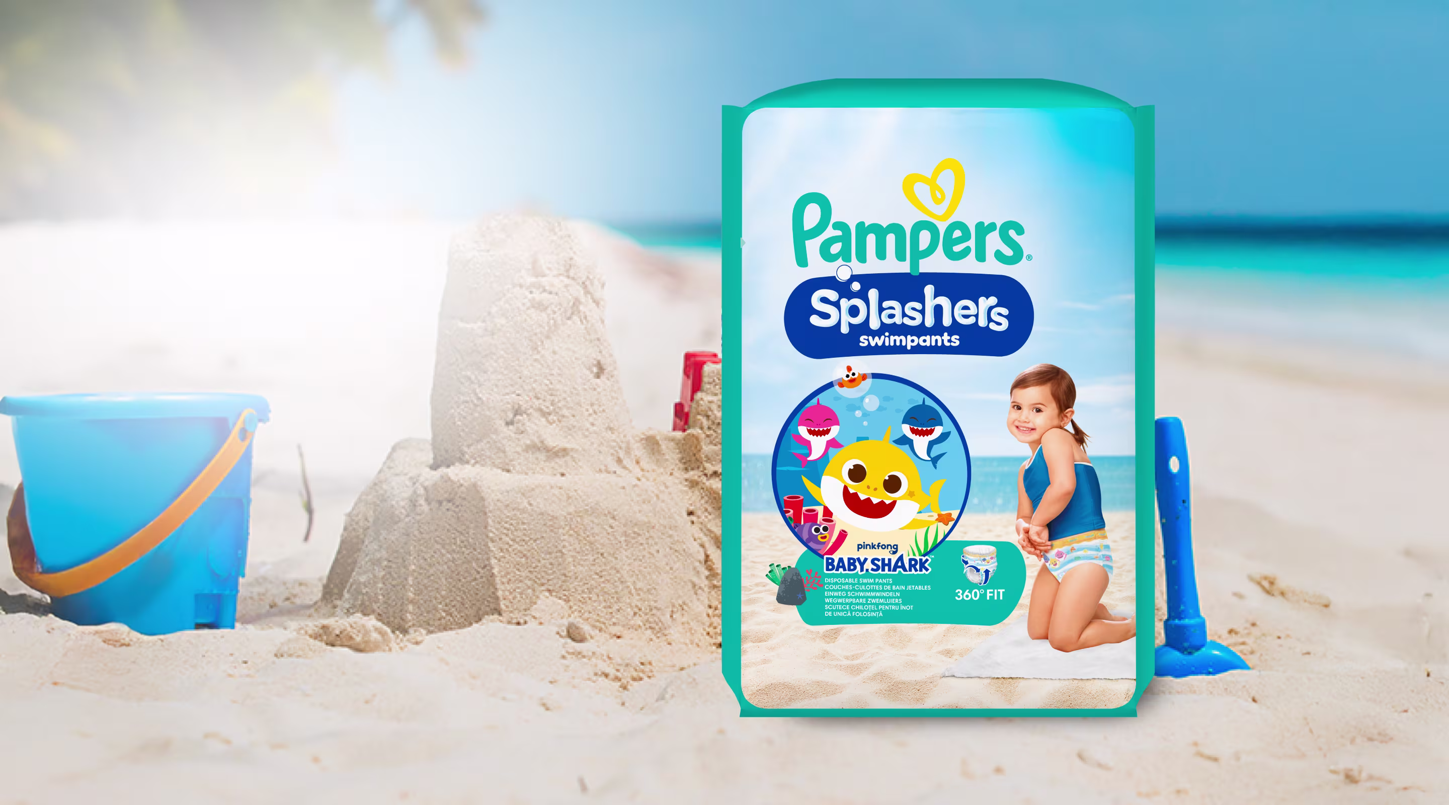 Eine Packung Pampers® Splashers Schwimmwindeln am Strand umgeben von Sandspielzeug.