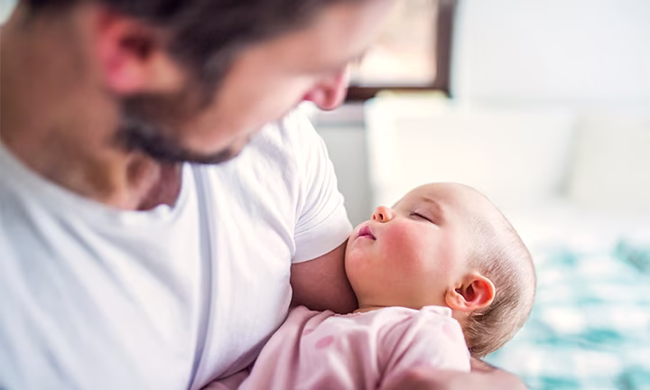 Dad and newborn bonding as a smiling father holds his baby close to his chest, both appearing relaxed and content in a warm home environment.