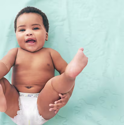 Ein fröhliches Baby liegt in einer hellblauen Decke und trägt eine Windel. Es lächelt und hebt spielerisch ein Bein, wodurch eine fröhliche und lebhafte Atmosphäre entsteht.