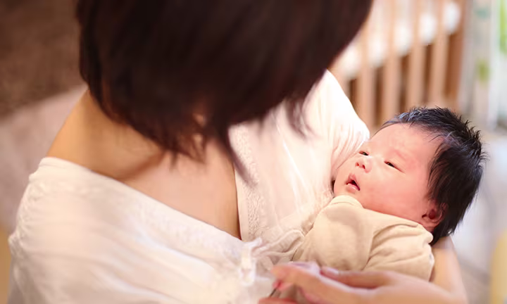 A caregiver holding a newborn baby in their arms while looking down at the baby’s face