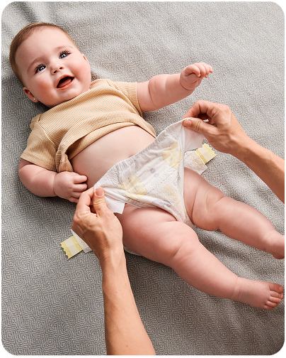 A joyful baby smiles as their parent gently secures a fresh diaper, ensuring comfort and care.