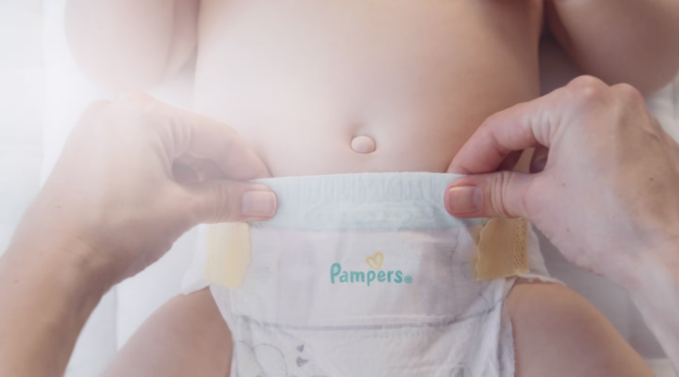 Eine Nahaufnahme zeigt zwei Hände, die vorsichtig das Bauchbündchen einer  Pampers-Windel auseinanderziehen und dabei das flexible & schützende Bauchbündchen demonstieren.