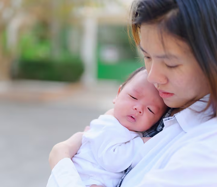 Mother gently cradling her sleeping baby outdoors.