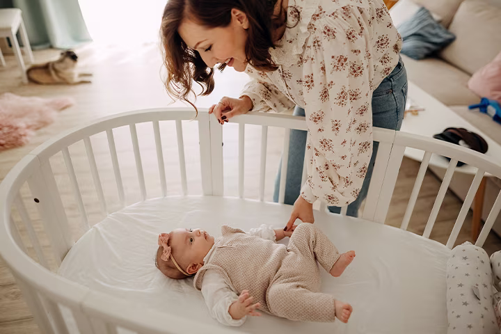 Femeie aplecată deasupra unui pătuț, mângâindu-și bebelușul  cu blândețe.