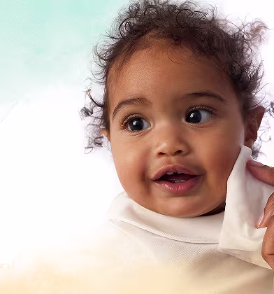 Prim-plan cu fața unui bebeluș, în timp ce o mână îi șterge ușor obrazul cu un șervețel umed Pampers Harmonie Protect & Care.