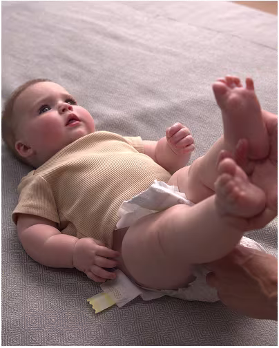 Um bebé alegre sorri enquanto o pai lhe tira a fralda, preparando-se para uma troca de fralda.
