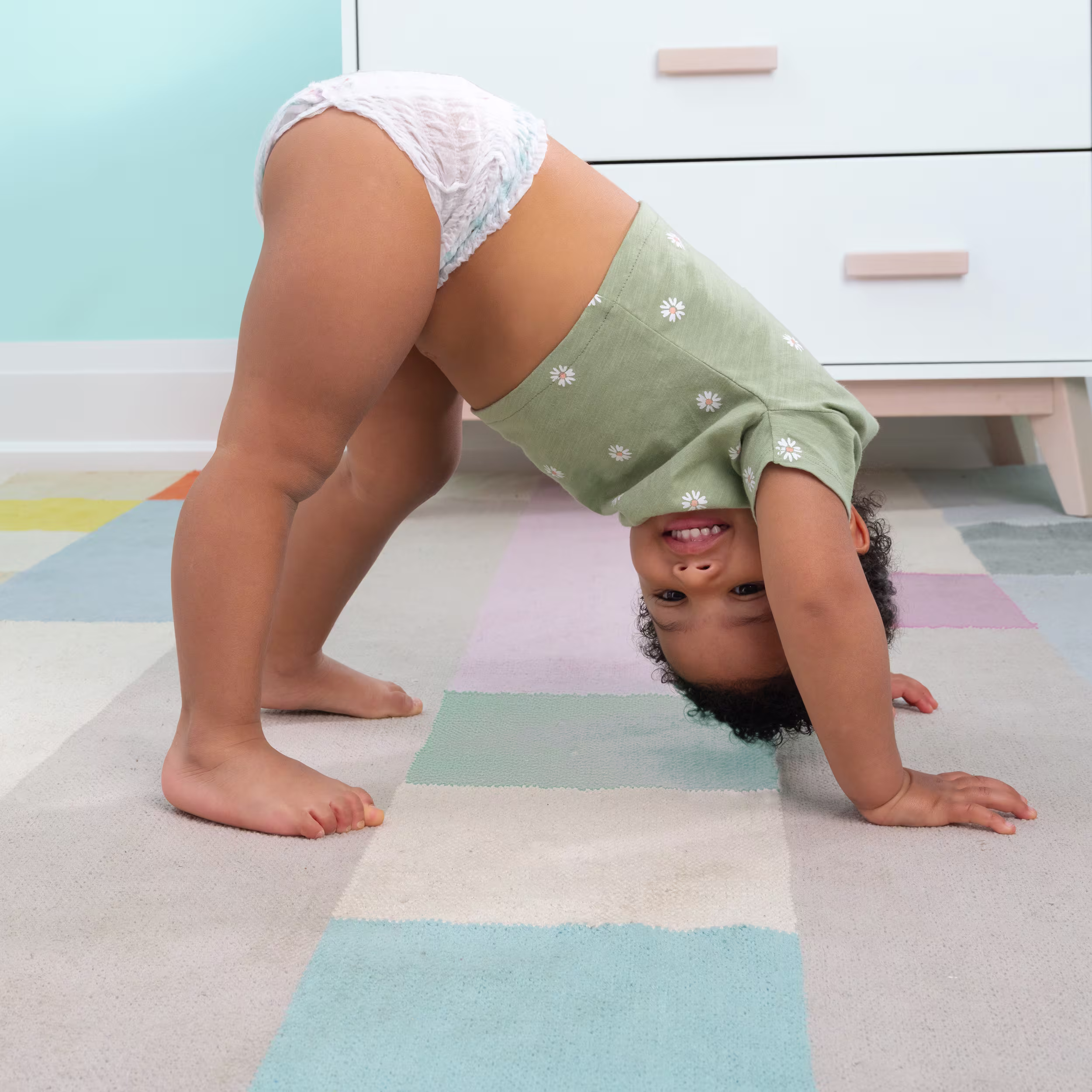Toddler wearing Pampers Cruisers360 doing downward dog stretching pose in nursery