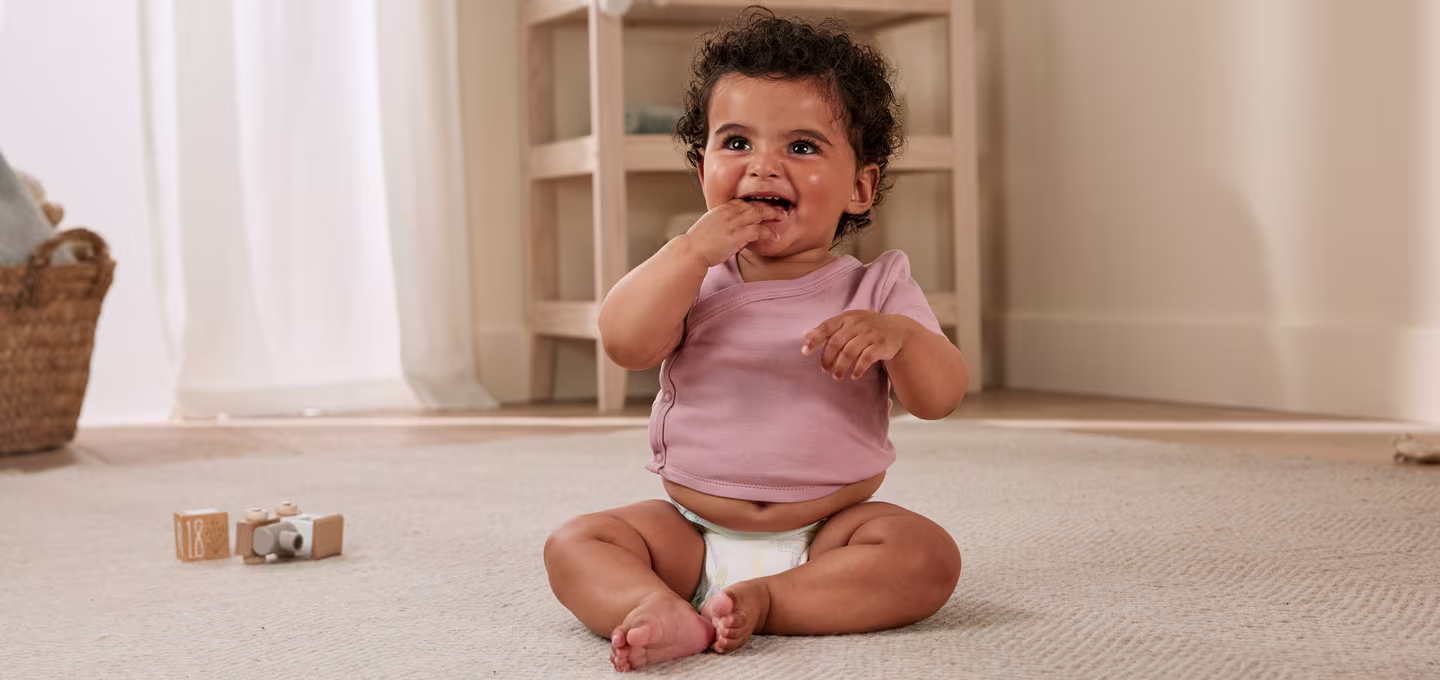 A baby wearing a diaper, sitting on the floor.