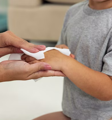 Acercamiento de una mamá limpiando suavemente la mano de su hijo con una toallita húmeda