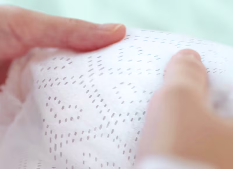 A close-up shot shows two hands gently holding a soft-textured Pampers nappy, highlighting its dotted pattern and plush feel