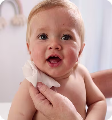Lähikuva vauvan kasvoista samalla kun käsi pyyhkii varovasti heidän poskeaan Pampers Harmonie Aqua -pyyhkeellä.