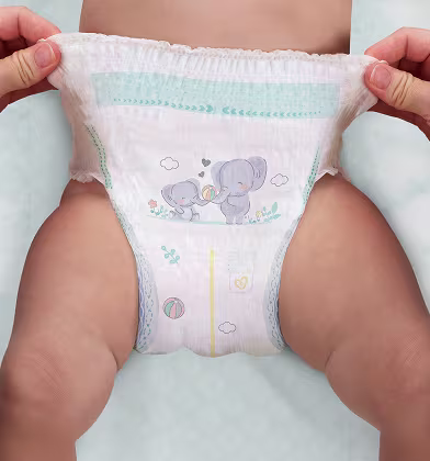 En baby som har på sig en vit blöja drar med två händer i den övre kanten av blöjan och sträcker ut den.