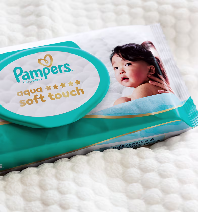 Het pak Aqua Soft Touch doekjes ligt op een omslag die de zachte honingraatstructuur van het vochtige doekje toont.